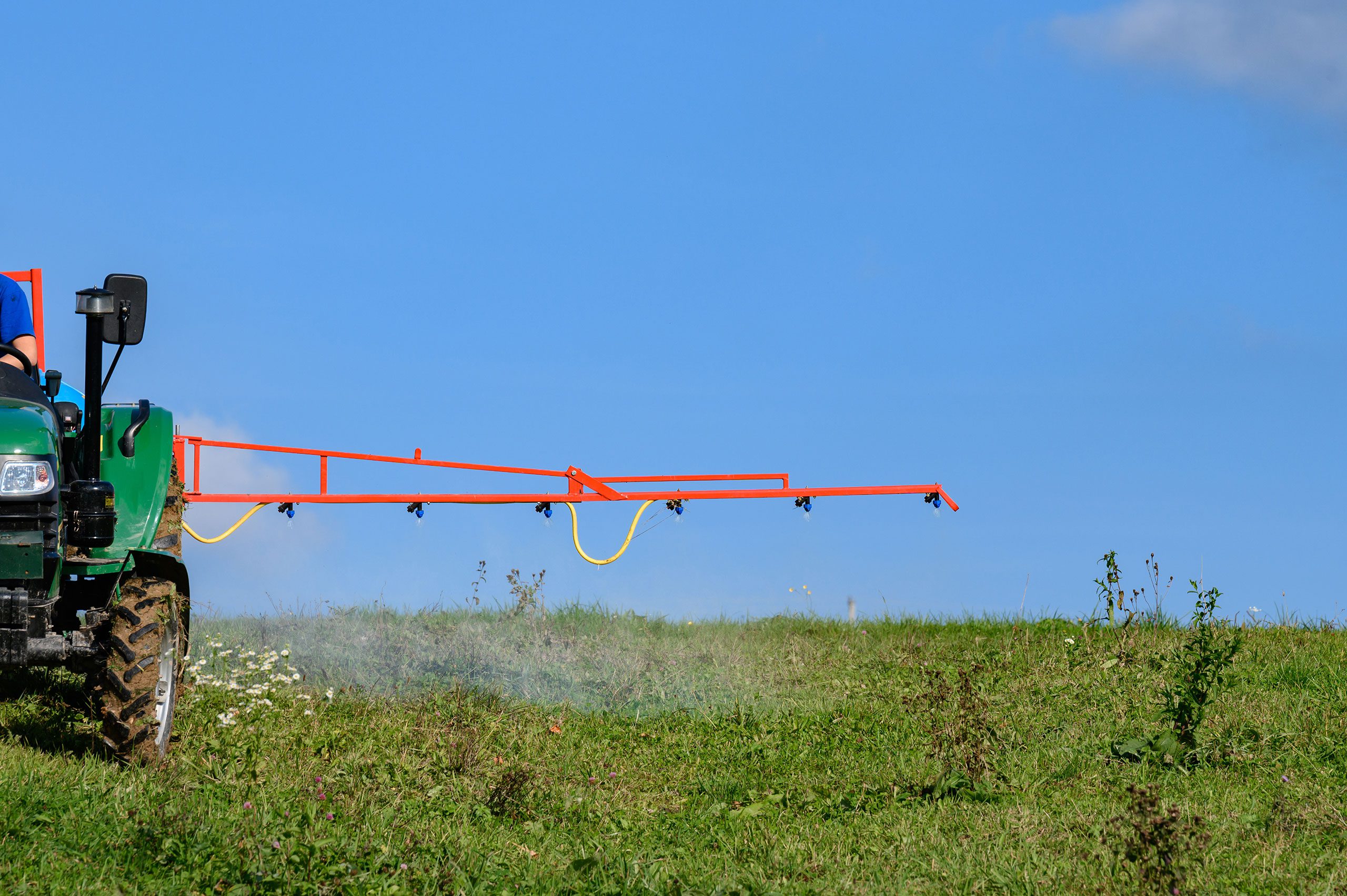 Tracteur agricole pulvérisant un champ, illustrant l’usage d’herbicides liés aux OGM