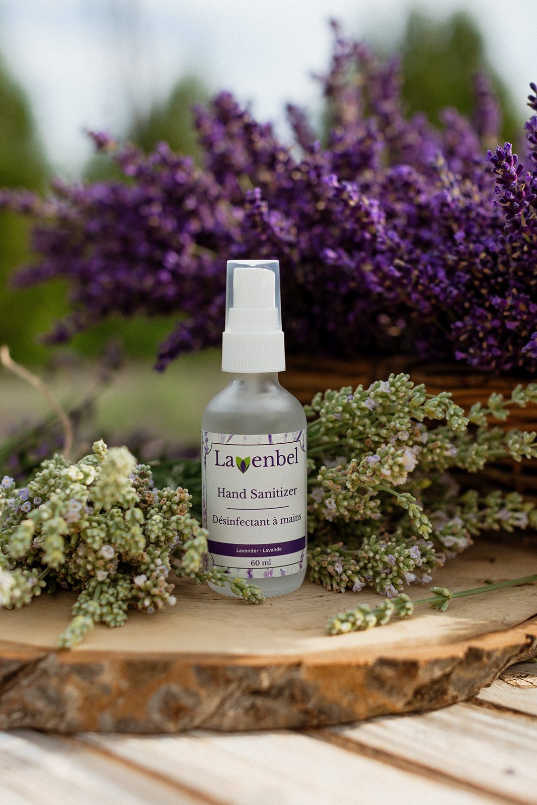 Lavender hand sanitizer (Lavenbel, 60 ml) on a wood slice, surrounded by lavender sprigs.